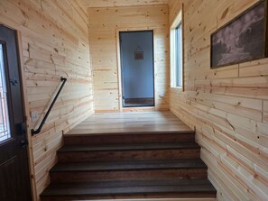 A wooden interior with a staircase leading to a door, a window, and a framed picture on the wall.
