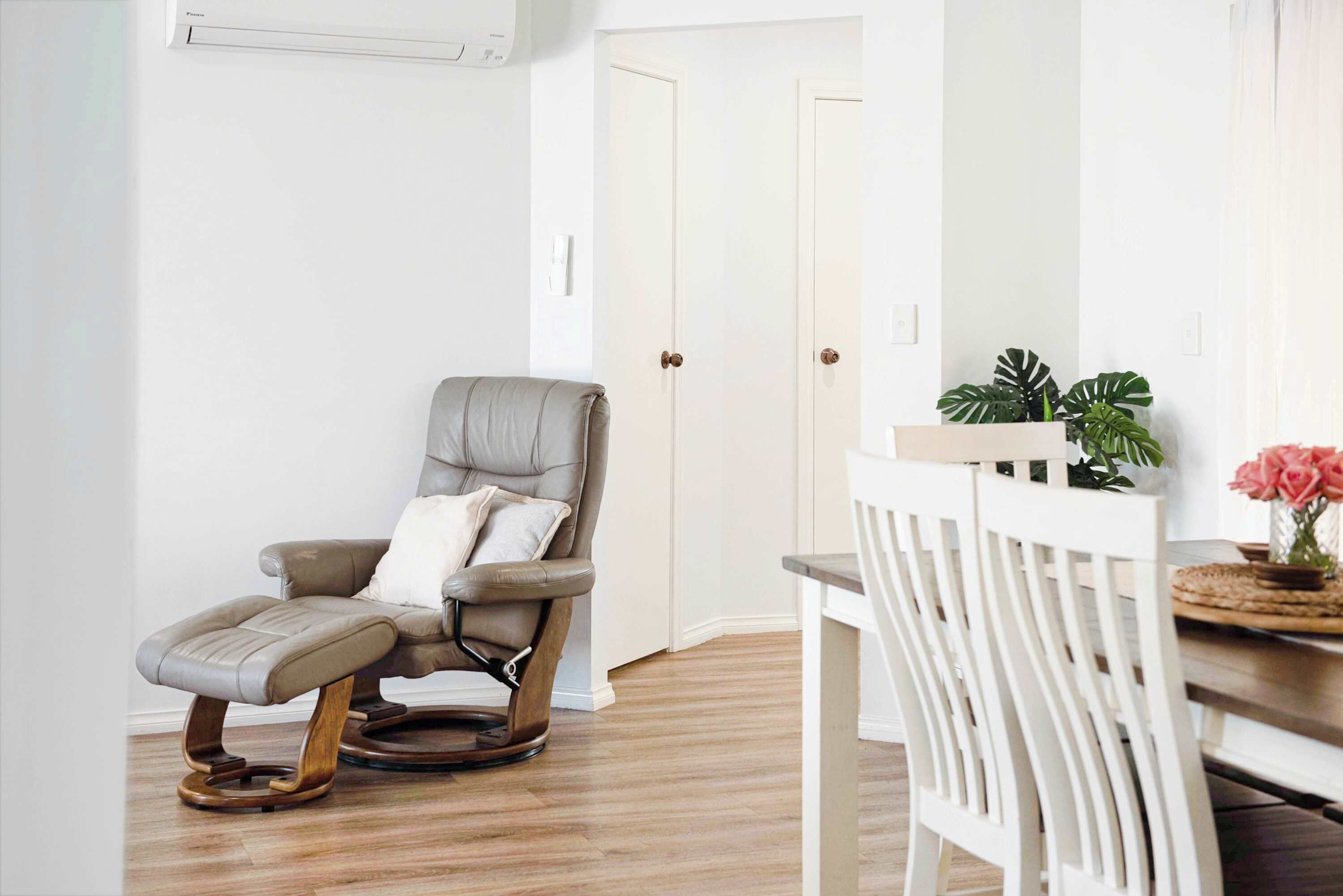 A room with a massage chair, a white dining table with chairs, and a potted plant.