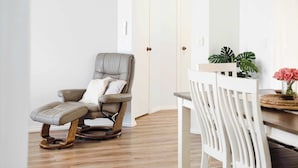 Una habitación con una silla de masaje, una mesa de comedor blanca con sillas y una planta en maceta.