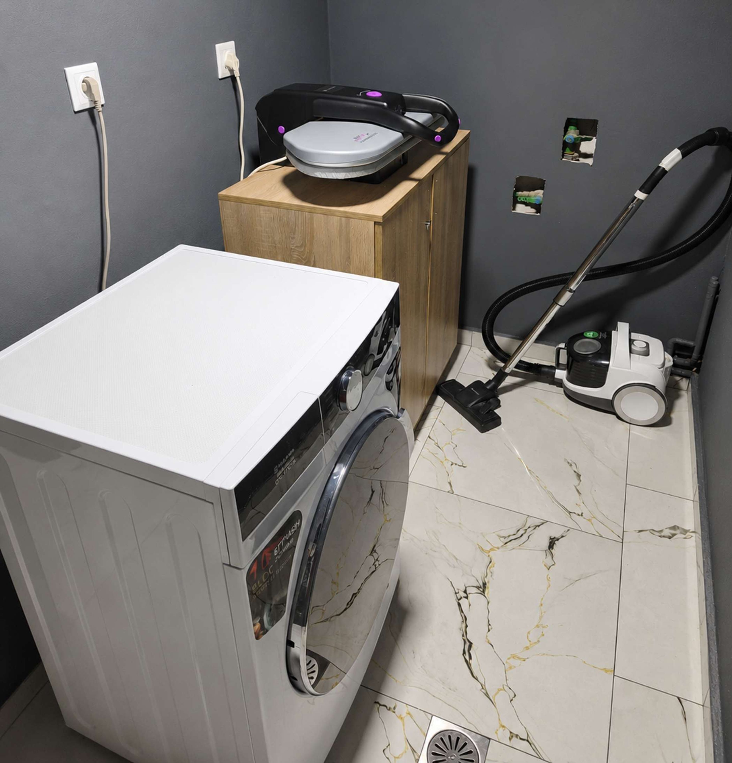 A laundry area with a washing machine, a vacuum cleaner, and a wooden cabinet.