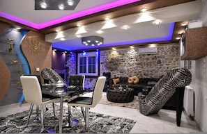 A modern living room with a glass dining table, black and white patterned sofa, and a stone accent wall.