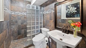 Un baño con cabina de ducha de vidrio, un inodoro, un lavabo y una obra de arte floral enmarcada sobre el espejo.