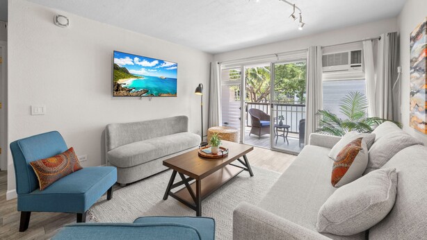 Una sala de estar con sofá, sillón, mesa de centro y un cuadro de una playa.