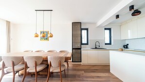 Een moderne keuken met een centraal eiland, een houten eettafel met stoelen, hanglampen en uitzicht op de eetruimte.