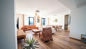 Een ruime woonkamer met een bank, fauteuil, bijzettafeltje en een kamerplant.