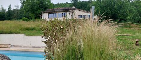 A house with a swimming pool, surrounded by greenery and a clear sky.