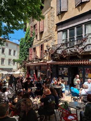 Ein Straßencafé mit Tischen und Stühlen, umgeben von Gebäuden mit sichtbarer Beschilderung.