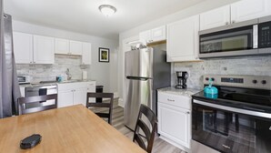 A modern kitchen with white cabinets, stainless steel appliances, and a wooden dining table. - The Grandstands Apt 2 - All Star Baseball Rentals (Oneonta)