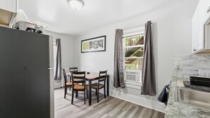 A compact kitchen with a dining area, a refrigerator, a sink, and a window with curtains. - The Grandstands Apt 2 - All Star Baseball Rentals (Oneonta)