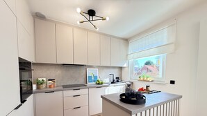Una cocina moderna con armarios blancos, una isla central, horno empotrado y ventana con vistas.