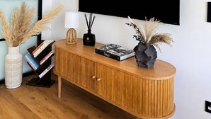 Una sala de estar moderna con una consola de madera, un televisor negro montado en la pared y decoración mural.