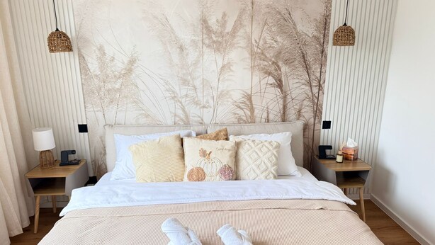 Una cama bien hecha con una colcha blanca texturizada, un cojín decorativo con diseño de calabaza y dos toallas enrolladas sobre la cama.