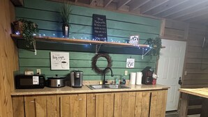 Une cuisine rustique avec des meubles en bois, un évier, un four à micro-ondes, une machine à café et une étagère ornée d’objets décoratifs.