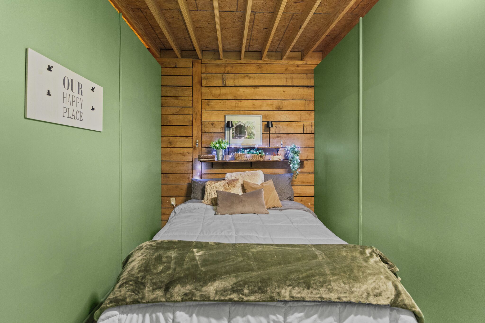 Una habitación con una cama, techo de madera, pared verde y un letrero que dice 'OUR HAPPY PLACE'.