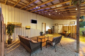 Un espacio interior con techo de madera, un televisor montado en la pared, una zona de comedor con mesa y sillas, y un área de estar con sofá y sillones.