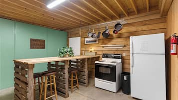 A kitchen with wooden walls, a stove, a refrigerator, and a bar stool.