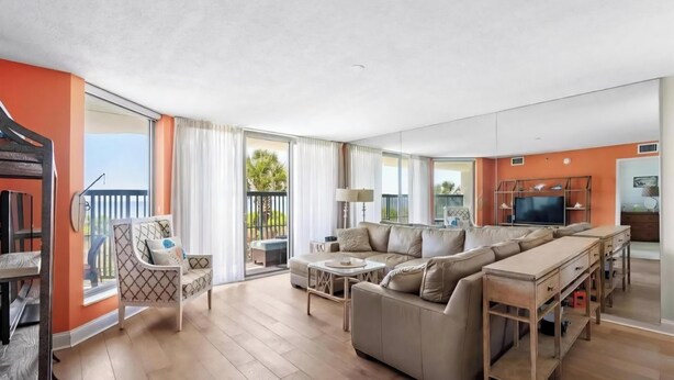 Ein modernes Wohnzimmer mit einer Sofagarnitur, einem Fernseher und einem Balkon mit Vorhängen.