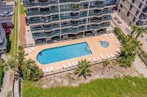 An aerial view of a hotel with a swimming pool, multiple balconies, and a parking area. - GOLF and BEACH PARADISE! Oceanfront 4-bedroom condo in nice North Myrtle Beach. (North Myrtle Beach)