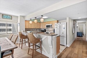 A kitchen with a central island, wooden cabinets, a microwave, a refrigerator, and a dining area with chairs. - GOLF and BEACH PARADISE! Oceanfront 4-bedroom condo in nice North Myrtle Beach. (North Myrtle Beach)