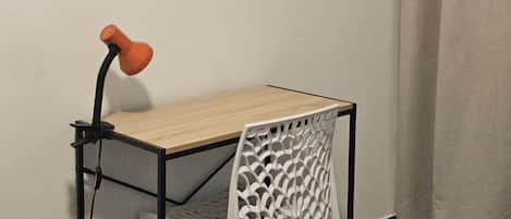 Une petite pièce moderne avec une table en bois et une chaise blanche, un miroir rond en osier accroché au mur et un rideau à la fenêtre.