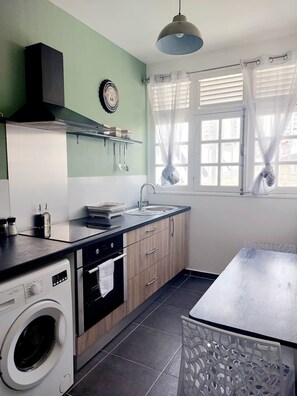 A compact kitchen with a washing machine, a sink, and a window with curtains. - Pearl at the heart of Pointe-à-Pitre (Pointe-a-Pitre)