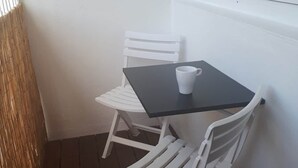 Ein kleiner weißer Tisch mit einer weißen Tasse, zwei weißen Stühlen und einem Fenster mit Jalousien.