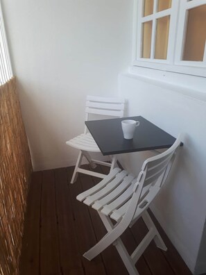Ein kleiner weißer Tisch mit einer weißen Tasse, zwei weißen Stühlen und einem Fenster mit Jalousien.