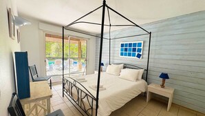 A bedroom with a four-poster bed, a desk, and a chair, a window with a view of the outdoors, and a nightstand with a lamp. - Villa forêt avec piscine privée | La plage à 2km (Moliets)