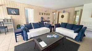 A living room with two sofas, a coffee table, a TV, and a door leading to another room. - Villa forêt avec piscine privée | La plage à 2km (Moliets)