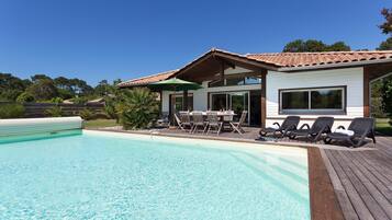 Ein modernes Haus mit Swimmingpool, einer Terrasse mit Stühlen und einem überdachten Außenbereich.