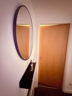 A room with a round mirror on the wall, a small shelf with a glass container, and a wooden door. - The Foregate Exchange (Worcester)