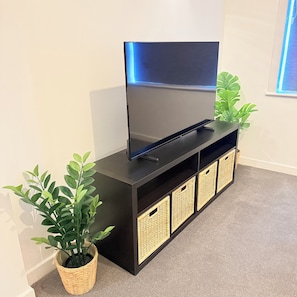 Uma televisão de tela plana sobre um móvel preto com cestos de vime e um vaso de planta.