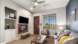 A living room with a fireplace, a television, a sofa, and a window with blinds. - Golf Course Views - Sleeps 4 - CLR 610-7 (La Quinta)