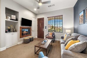 Ein Wohnzimmer mit Kamin, Fernseher, einer Couch und einem Fenster mit Jalousien.