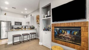 A modern kitchen with white cabinets, a built-in microwave, and a large flat-screen TV mounted above a fireplace. - Golf Course Views - Sleeps 4 - CLR 610-7 (La Quinta)