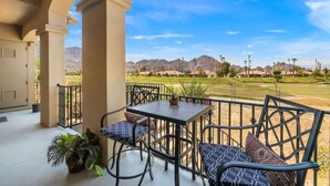 A covered outdoor seating area with a table and chairs, potted plants, and a view of a golf course and mountains. - Golf Course Views - Sleeps 4 - CLR 610-7 (La Quinta)