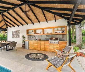 Een buitenkeuken met een barbecue, eettafel en stoelen.
