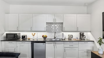 A modern kitchen with white cabinets, a stainless steel sink, a microwave, a toaster, and a coffee maker.