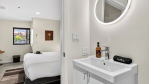 A hotel room with a bed, a bathroom with a sink and mirror, a window with a view, and a wall-mounted light fixture. - Red Rock Nook by Avantstay West Sedona Retreat Near Trails + Dining + Mountain Views (Sedona)