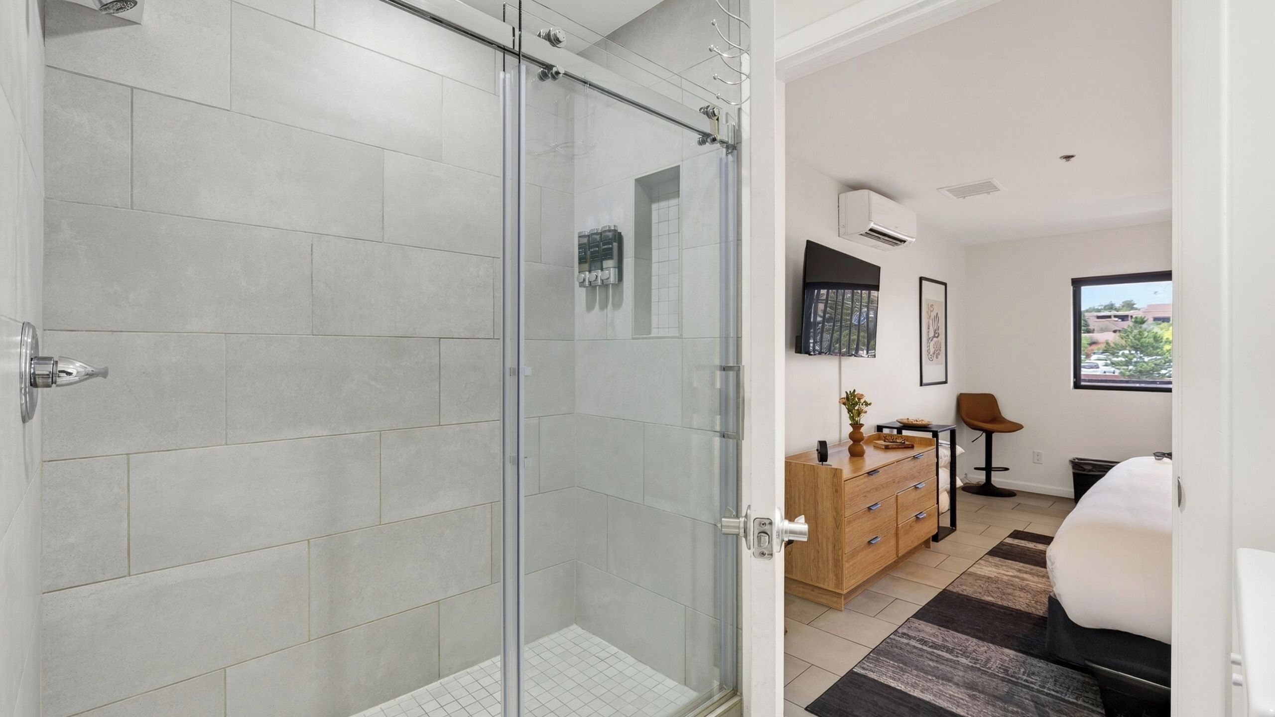 A modern bathroom with a glass shower enclosure, a wooden vanity, and a view of the outdoors through a window.