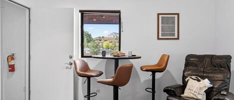 Una habitación con puerta, ventana con vistas, dos sillas, una mesa y un sofá.