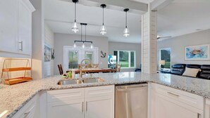 Una cocina moderna con gabinetes blancos, encimeras de granito, lavavajillas de acero inoxidable e iluminación colgante.