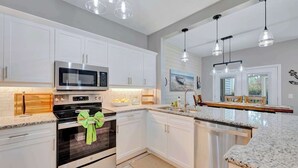 Una cocina moderna con armarios blancos, electrodomésticos de acero inoxidable e iluminación colgante.