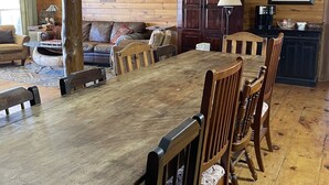 Een houten eettafel met stoelen, een bank, een koffiehoek en ingelijste foto’s aan de muur.