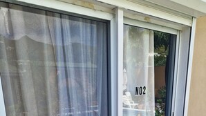 Een schuifdeur van glas met het nummer '02', een witte buitenmuur en een ventilatieopening in de grond.