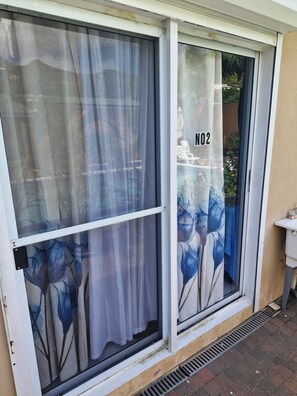 A sliding glass door with a number '02' on it, a white exterior wall, and a vent on the ground. - Cozy, convenient and secured studio-Located Almond Grove Cole bay. (Cole Bay)