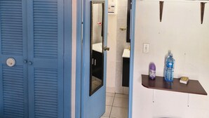 Een kamer met een gesloten blauwe deur, een wit wastafel, een spiegel, een televisie en een waterfles op een klein tafeltje.