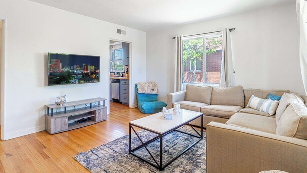 A living room with a sofa, coffee table, TV, and a view of a cityscape through a window. - Midtown Sanctuary w Pac-Man! (Reno)