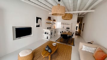 Una sala de estar moderna con televisor, sofá, mesa de centro y una zona de cocina con mesa de comedor.
