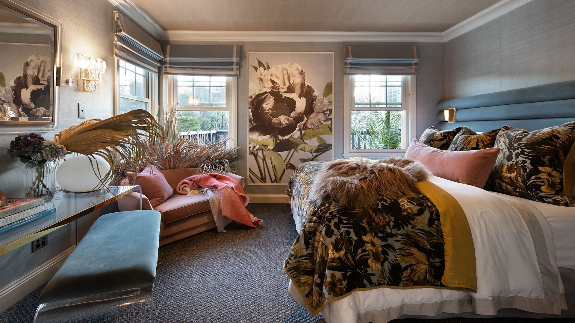 A bedroom with a large bed, a desk, a chair, and a window with a view of greenery.